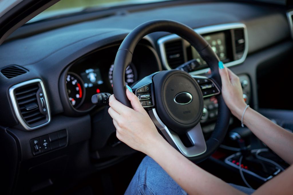 Close-up of a woman's hands on a steering wheel in a modern car interior.