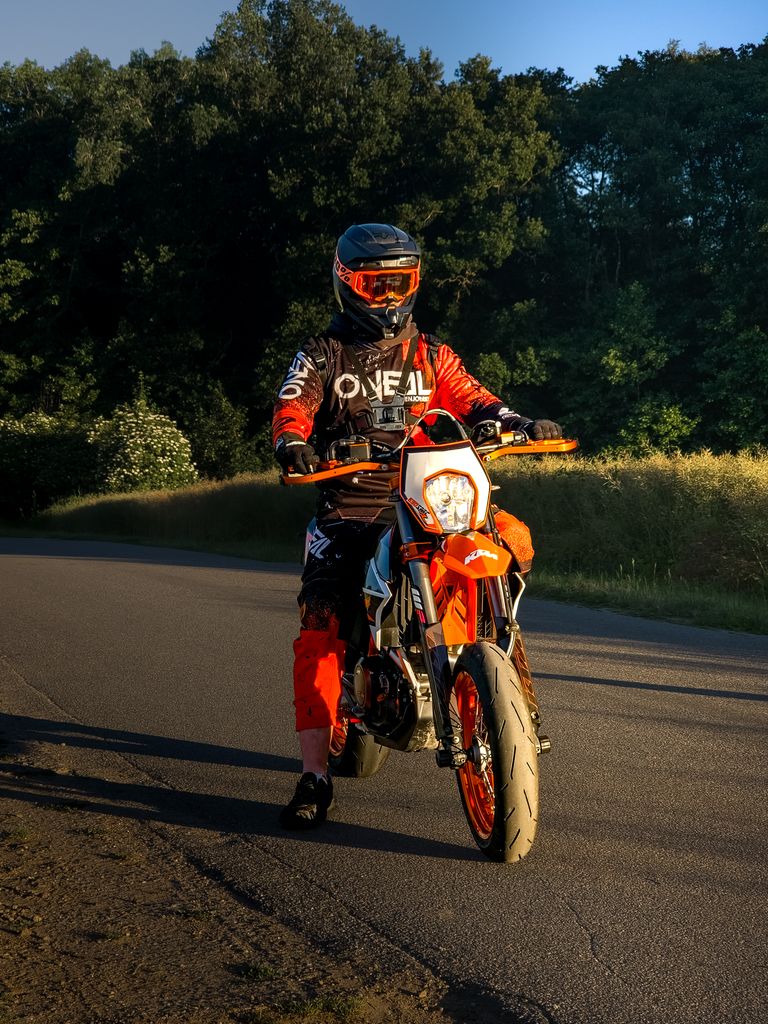 Motorcyclist in protective gear rides along a serene rural road during sunset, showcasing adventure and freedom.